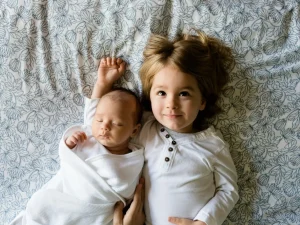 A little girl and her baby sibling laying on the floor together.