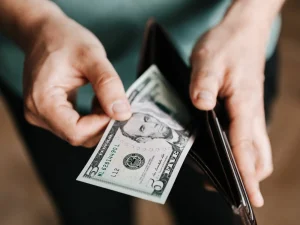 A man pulling a 5 dollar bill out of his wallet.