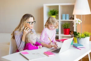 A mom works at her desk while her two daughters help her.