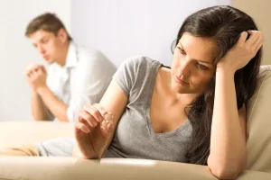 A woman and man sit separated while she looks at her wedding ring considering divorce.