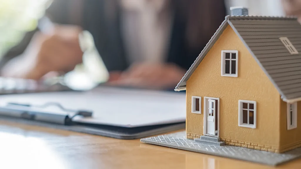 A toy house sitting next to someone writing on documents.
