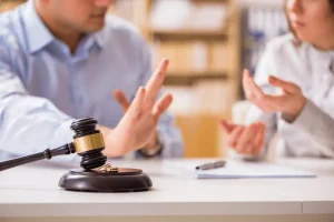 Two people in a disagreement with the scales of justice in the foreground and wedding rings.