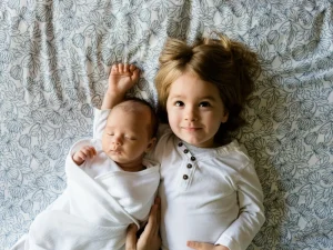 A child and their sibling laying happily on the bed.