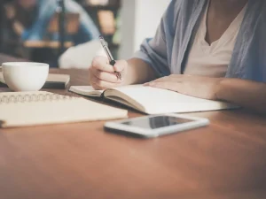 A woman writing in her journal and a cup of coffee.