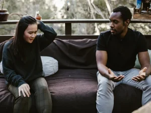 A couple sits across from one another and looks distraught and in disagreement.