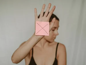 A woman looking away holding a paper with a "X" written on it.