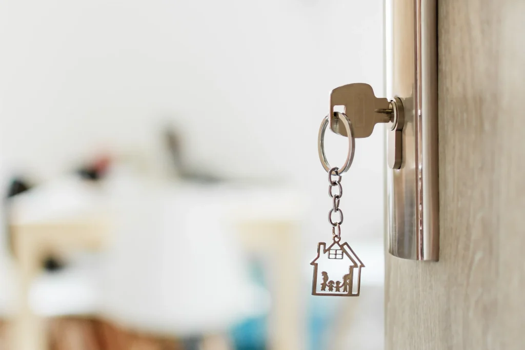 A key hanging in the lock of a door with the symbol of a house on the keychain.