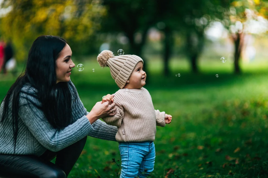 A mom and baby in the park blowing bubbles.