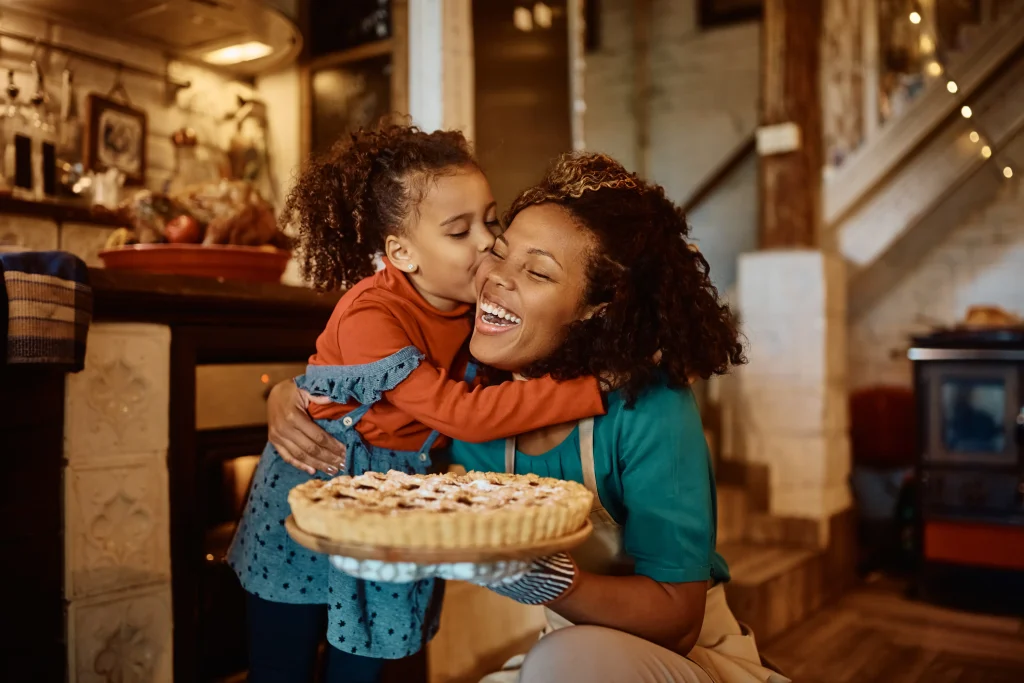 a mom and her daughter hugging and smiling while holding a fresh baked pie.