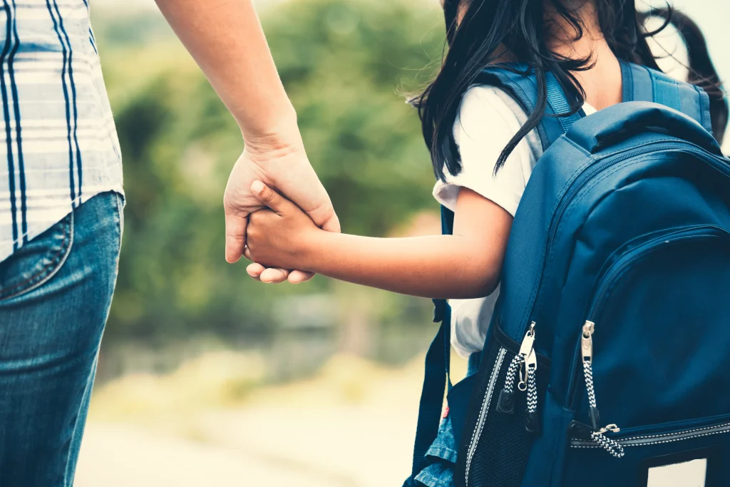 A mom with a child wearing a backpack walking and holding hands.