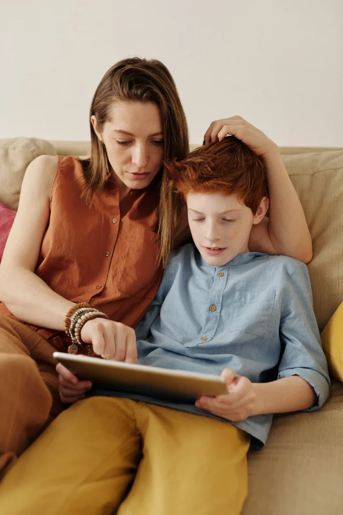 A mom sitting next her son while looking at the tablet together.