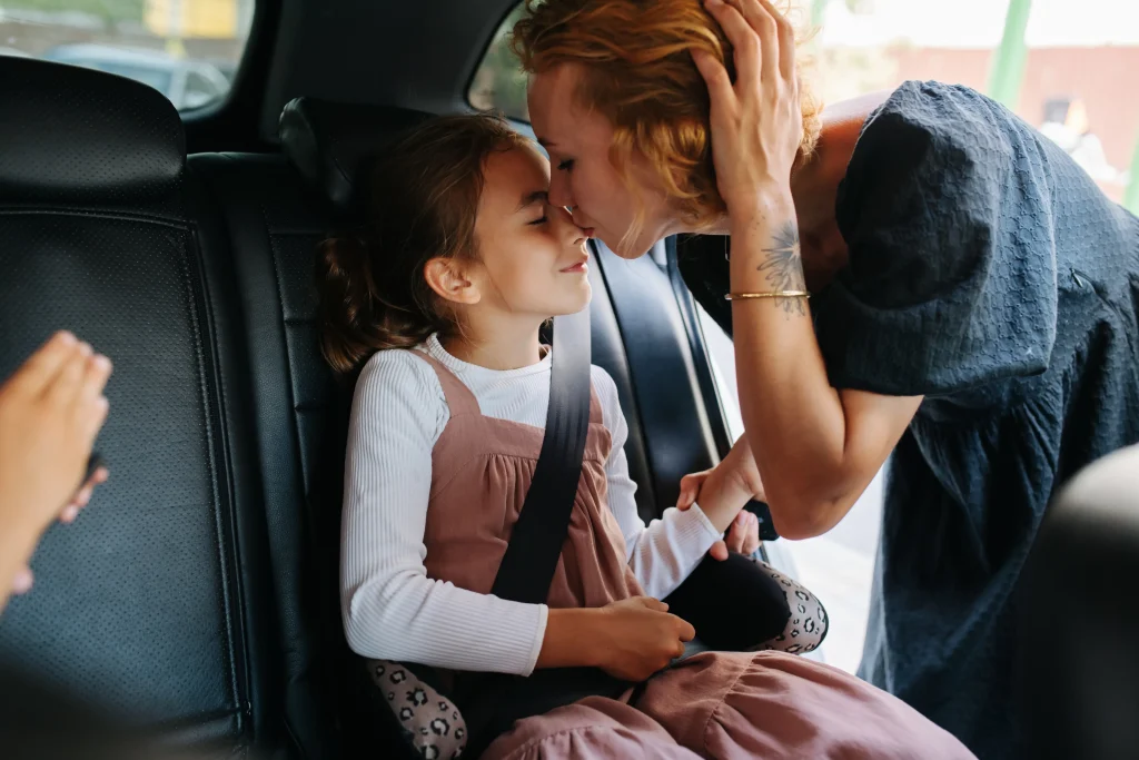 A mom kissing her daughter as she buckles her into the car.