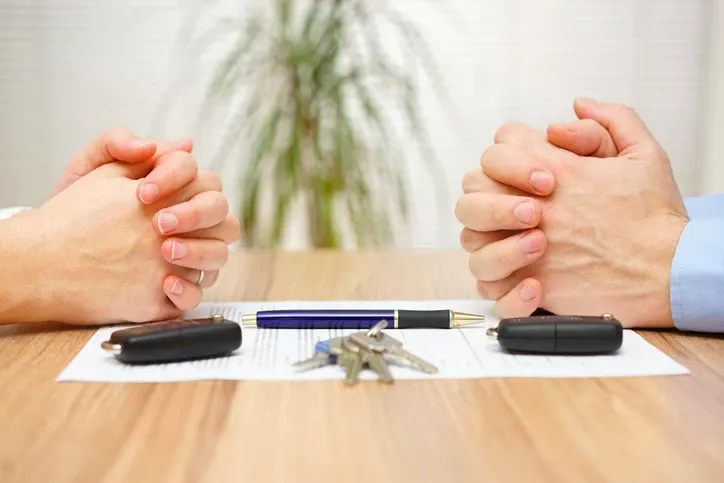 a man and woman with folded hands sitting at a table with keys and paperwork.