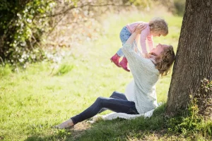 A mom holding up her child while sitting outside.
