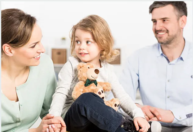 Parents sitting with their child who is holding a teddy bear.