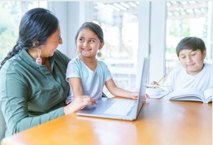 A mom working at the table with her two kids.