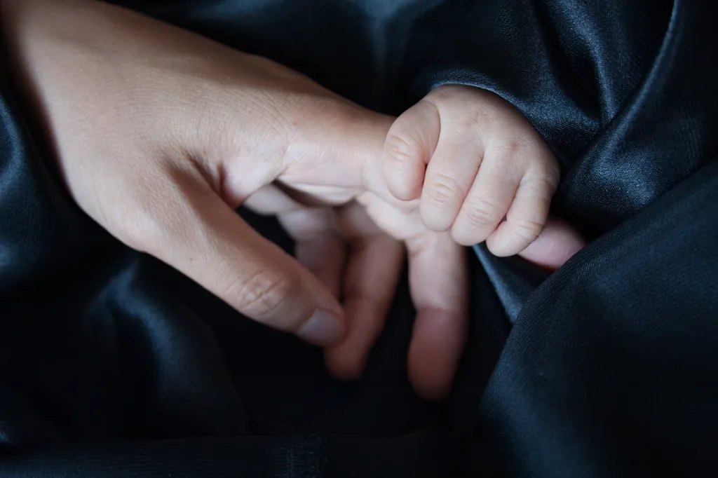 A baby's hand holding his mom's finger.