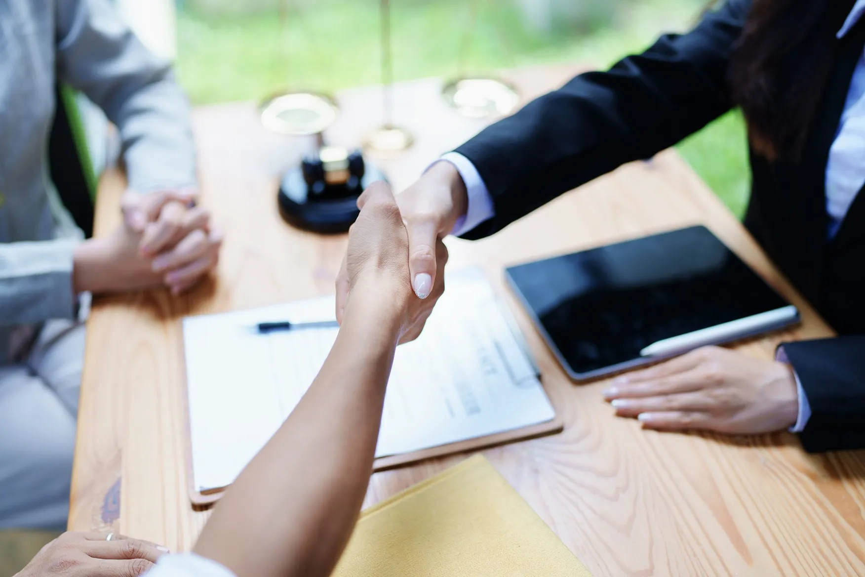 Two people shaking hands with papers on a desk.