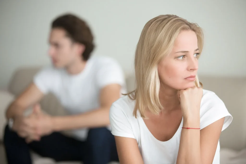 A woman with her head on her hand looking concerned with a man sitting behind her.