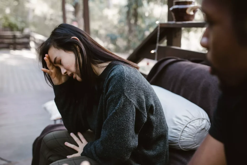 A distressed woman with her hands placed on her forehead sitting next to a man.