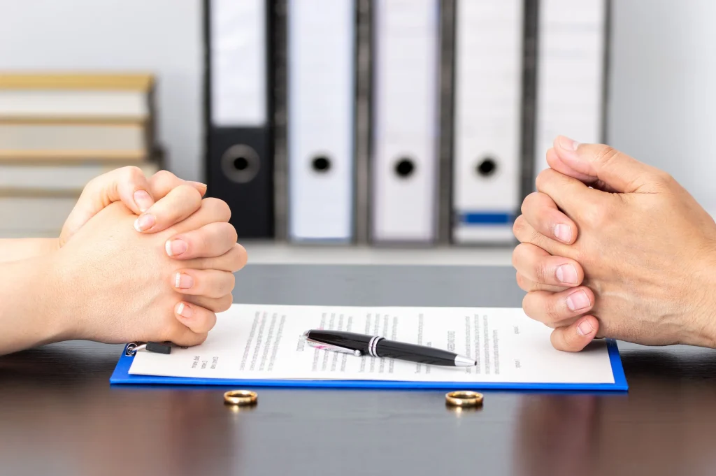 Two people crossing their hands sitting at a table with divorce papers.