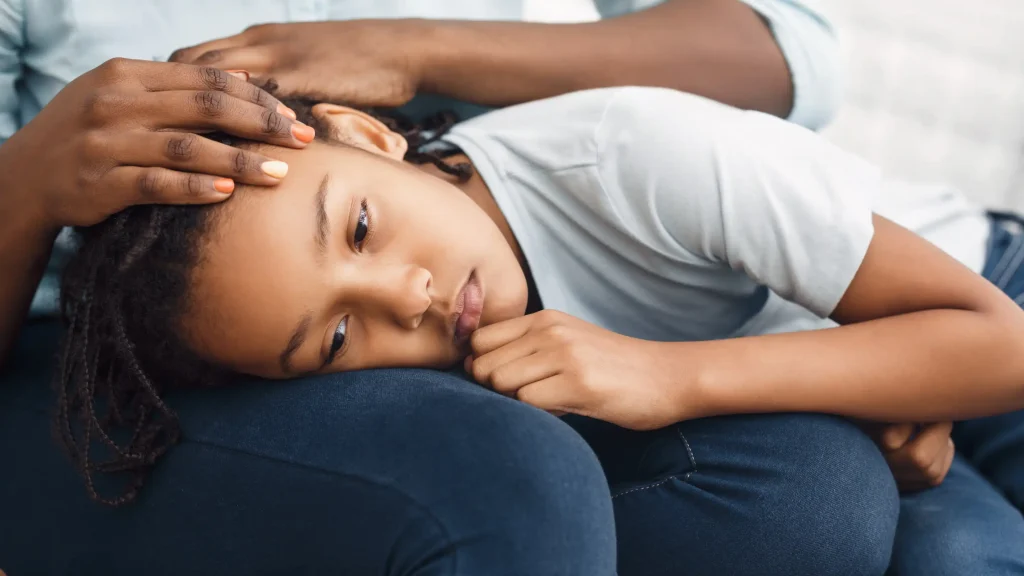 Close-up of a sad young girl resting her head on her mother's lap.
