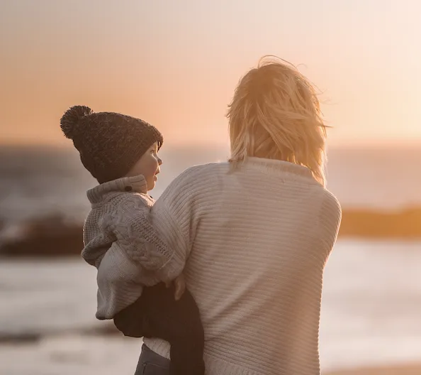 A mother holding her baby on her hip during a sunrise.
