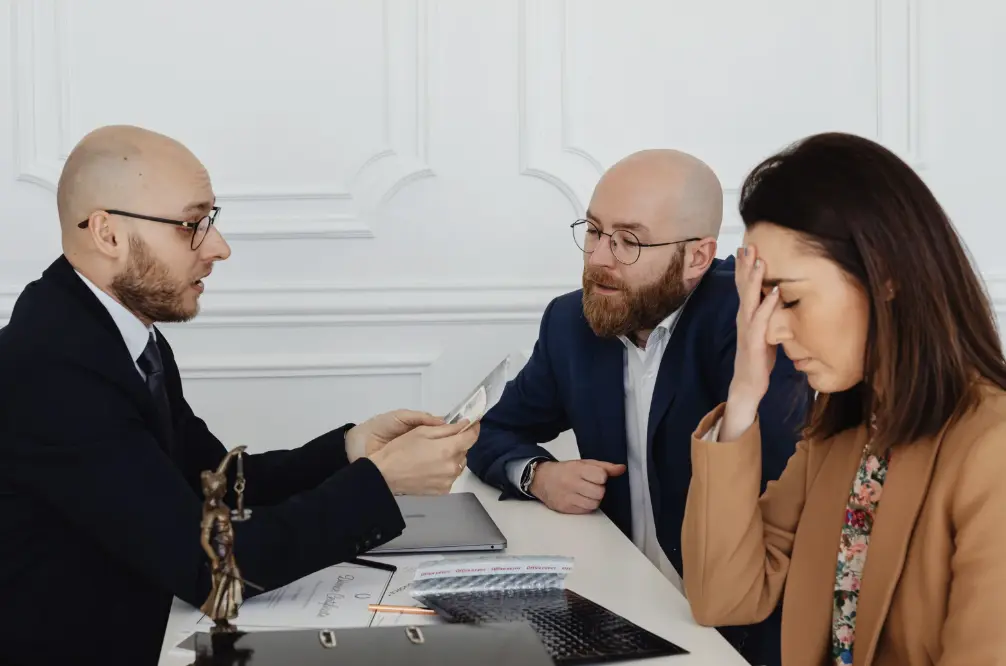 A lawyer shows a document to a stressed woman and her partner in a high-conflict divorce.