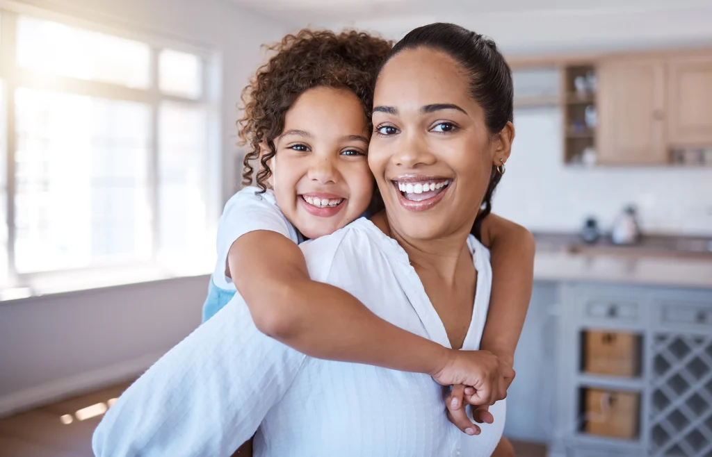 A smiling mother giving her happy daughter a piggy back ride.