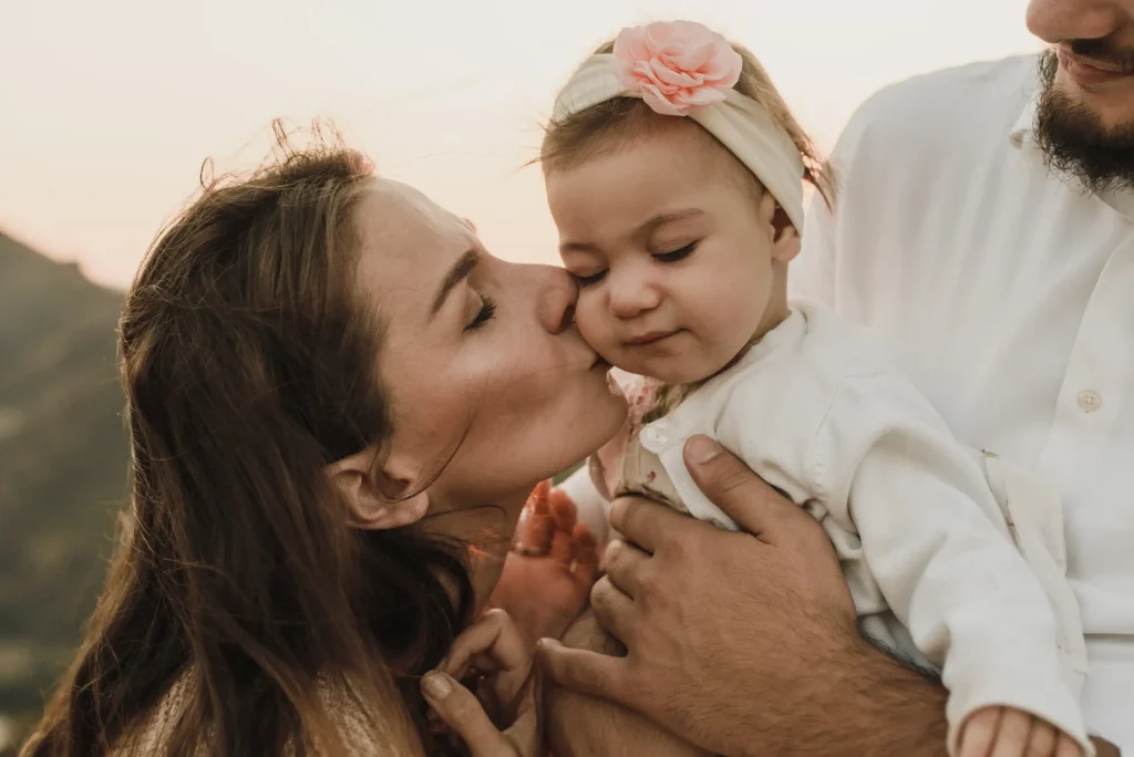 A mom kissing her baby daughter on her cheek.